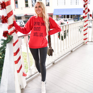 Woman standing on a holiday-decorated porch wearing a red “Dear Santa” sweatshirt with black leather leggings and white studded boots.

