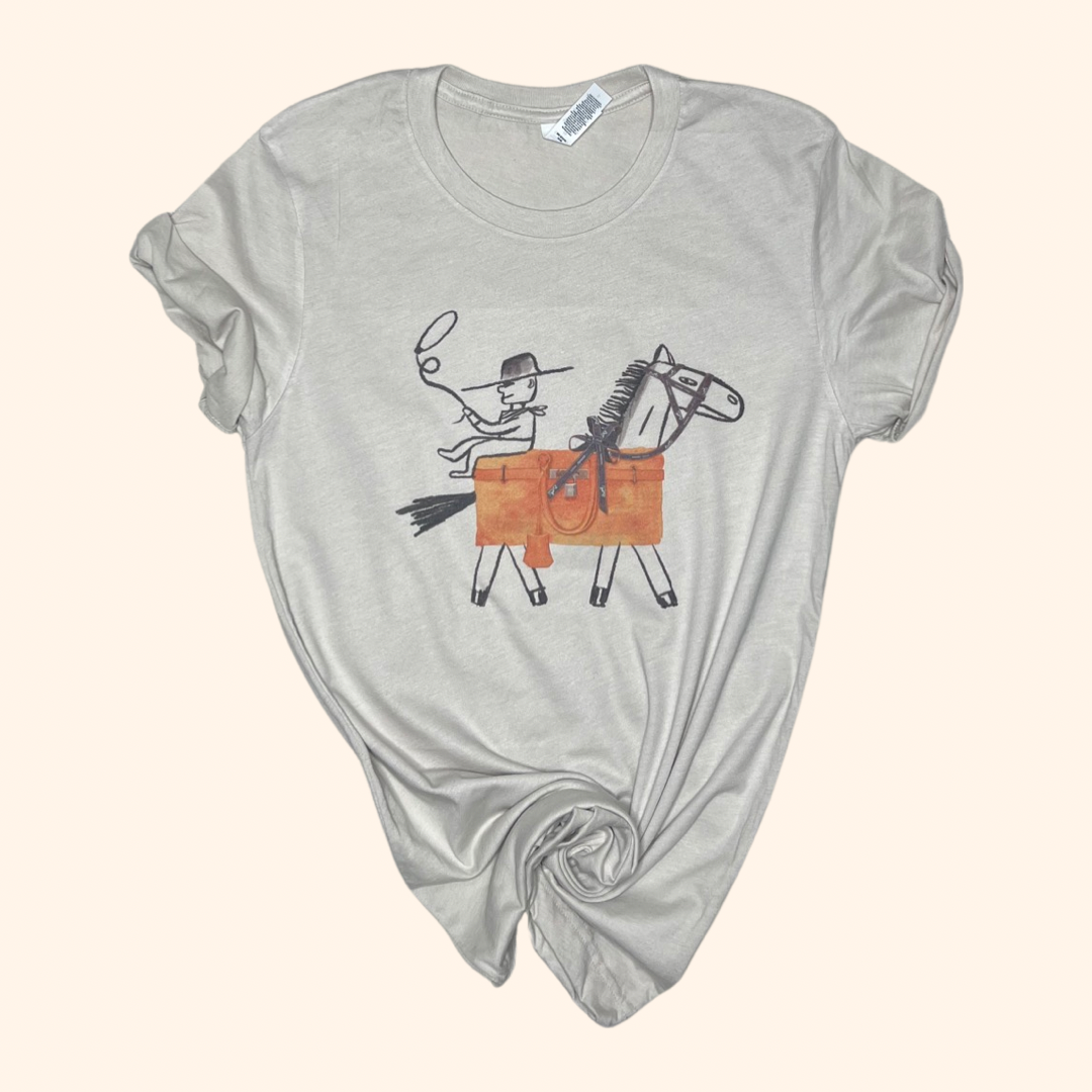Beige Western graphic tee with cowboy and horse design, laid flat with rolled sleeves and a knotted hem.