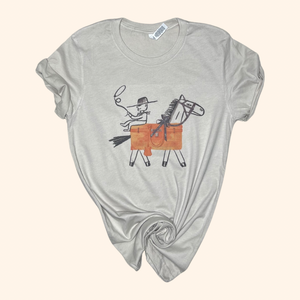 Beige Western graphic tee with cowboy and horse design, laid flat with rolled sleeves and a knotted hem.