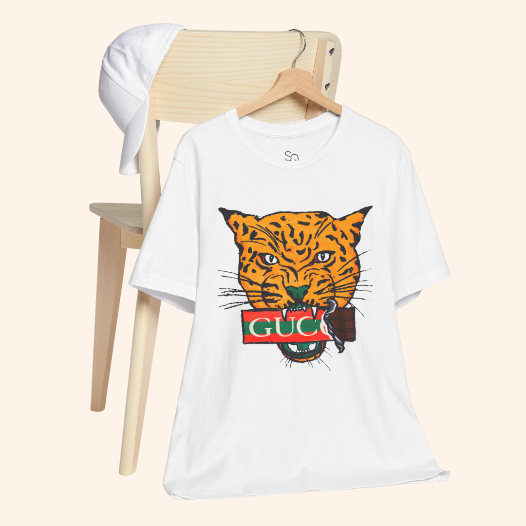All Mine Street Style Graphic Tee hanging on wooden chair with white cap, minimalist aesthetic featuring bold orange tiger design