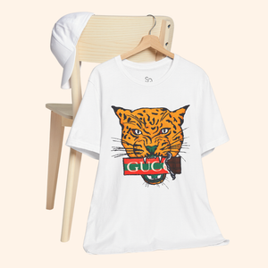All Mine Street Style Graphic Tee hanging on wooden chair with white cap, minimalist aesthetic featuring bold orange tiger design