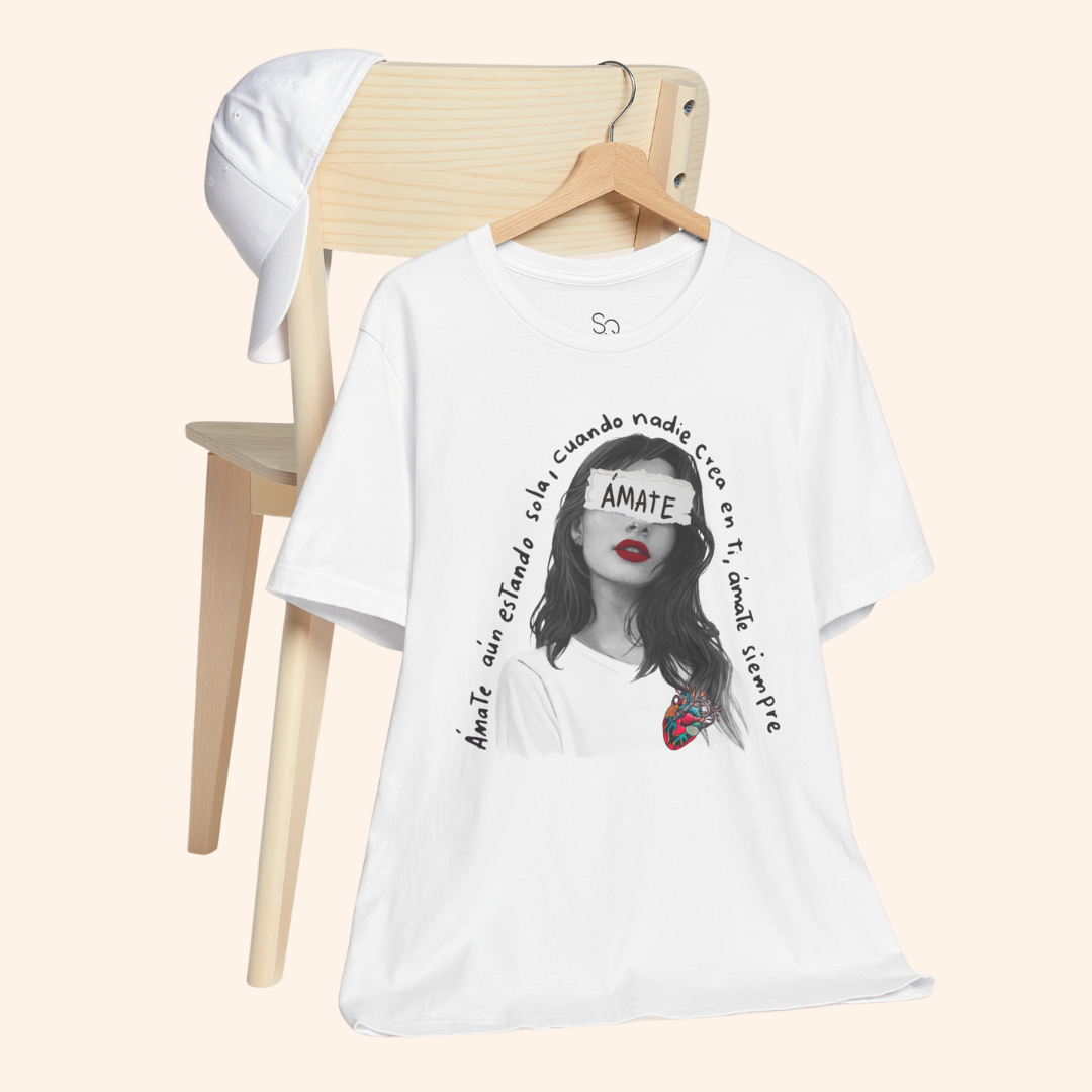 White Amate t-shirt hanging on wooden chair next to white cap, minimalist aesthetic emphasizing everyday wearability and lifestyle appeal.
