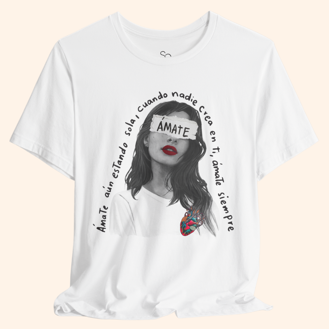 Close-up of white graphic t-shirt featuring a black-and-white portrait with red lips, colorful heart detail, and Spanish text “Ámate aún estando sola cuando nadie cree en ti, ámate siempre.” Inspirational design promoting self love.