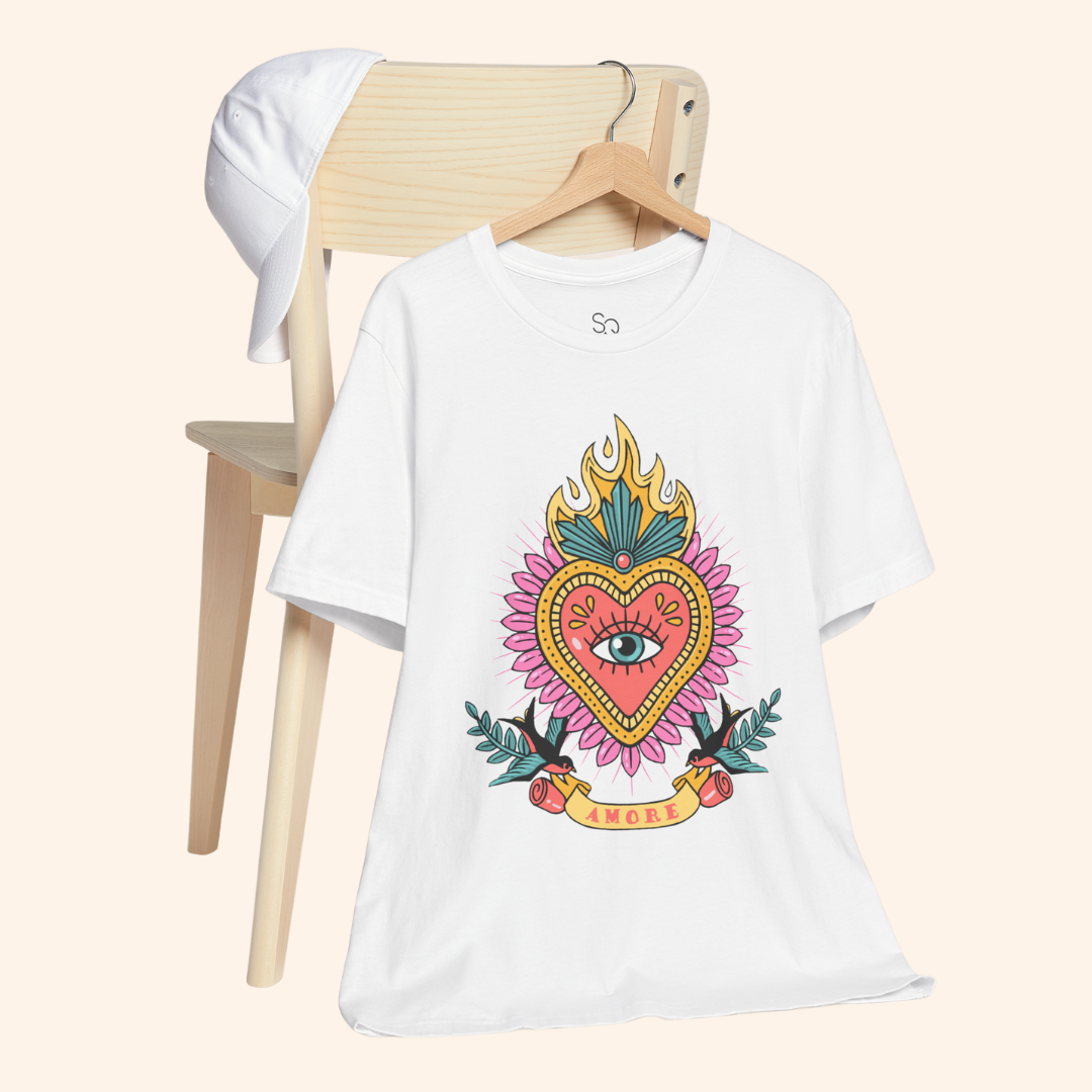 White sacred heart graphic tee hanging on wooden chair with cap nearby; relaxed lifestyle styling for street style fashion look.