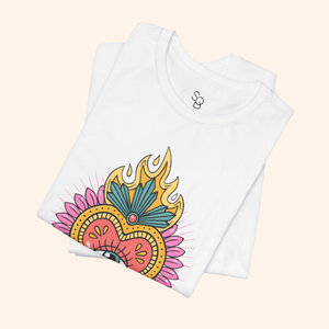 Folded white cotton tee showing upper portion of sacred heart with flames and teal feather accent; minimalist product detail for graphic tee.