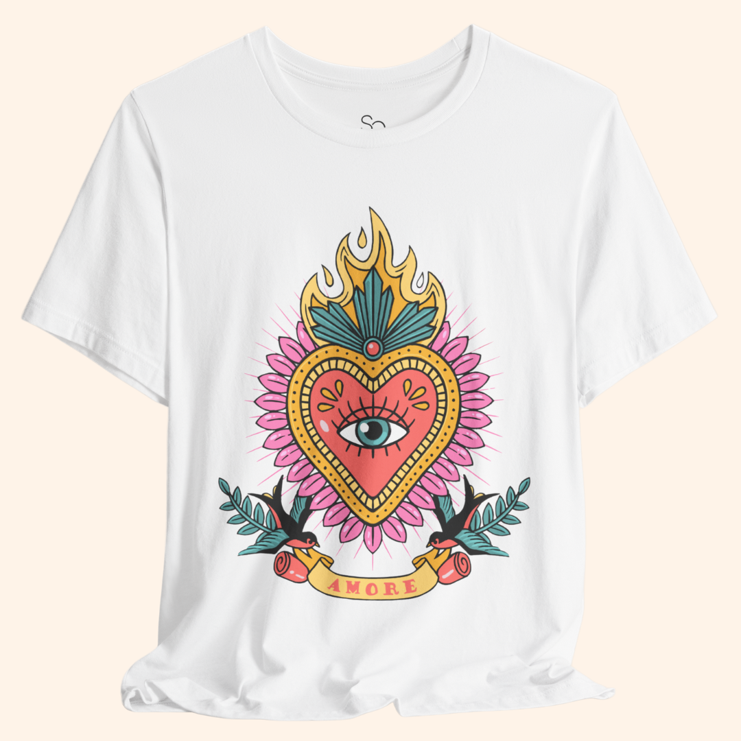 Closeup of white Amore T-Shirt showing sacred heart graphic with flaming crown, teal feather detail, and central eye motif; street style graphic tee.