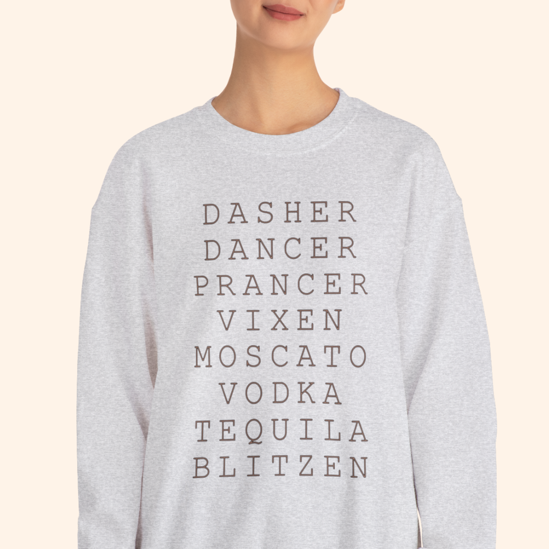 Tight chest-up view of a heather gray crewneck showing stacked black lettering that reads DASHE R DANCER PRANCER VIXEN MOSCATO VODKA TEQUILA BLITZEN; clean neutral background highlighting print detail and fabric texture.