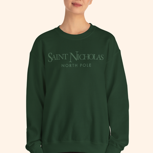 Woman wearing forest-green Saint Nicholas Christmas Sweatshirt with minimalist “North Pole” design across chest; relaxed fit, holiday streetwear style.