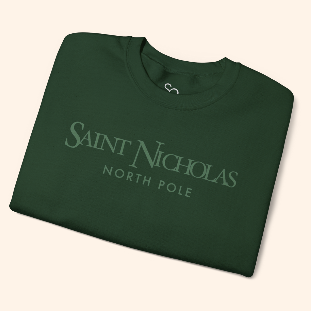 Forest-green Saint Nicholas Christmas Sweatshirt neatly folded on neutral background; soft cotton-poly fleece texture, minimalist holiday logo visible.