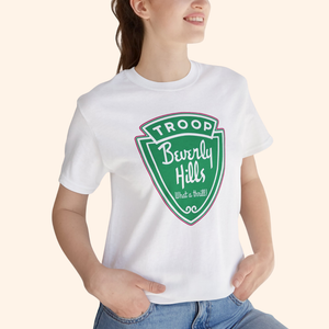Model wearing the white Troops graphic tee with the green retro badge design, styled casually with hands in pockets.