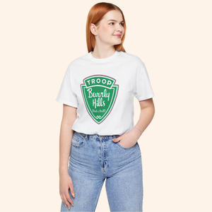 Mid size model wearing the Troops T-Shirt, white cotton top with bold green graphic, paired with light denim jeans.