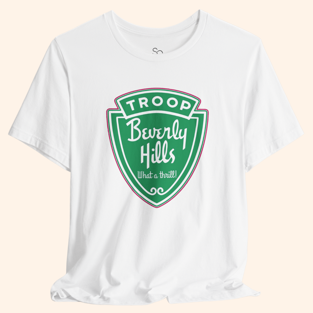 White graphic tee with a large green Troops Beverly Hills style badge print, bold retro lettering, soft cotton fabric, front centered design.