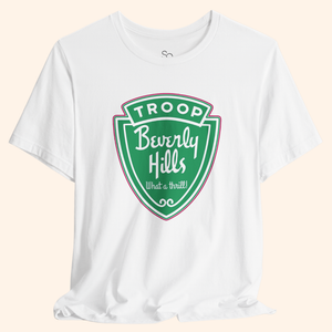 White graphic tee with a large green Troops Beverly Hills style badge print, bold retro lettering, soft cotton fabric, front centered design.