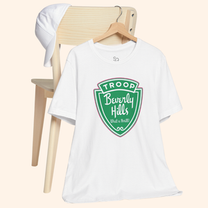 White Troops graphic tee hanging on a wooden chair next to a white cap, showcasing the green retro badge design and relaxed fit.