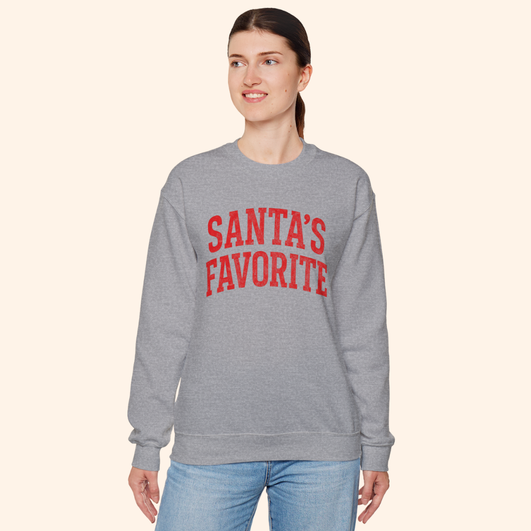 Full view of a woman wearing the Santas Favorite graphic sweatshirt with a comfortable unisex fit. Heather gray fleece with red lettering styled for an everyday holiday outfit that blends comfort and seasonal fashion.