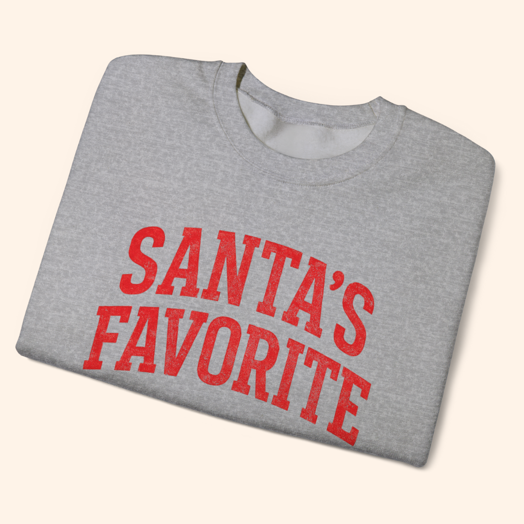 Heather gray Santas Favorite sweatshirt folded neatly to display the red graphic text across the chest. Shows the soft fleece material, ribbed collar, and clean finish, styled as a cozy holiday pullover perfect for gifting or winter outfits.