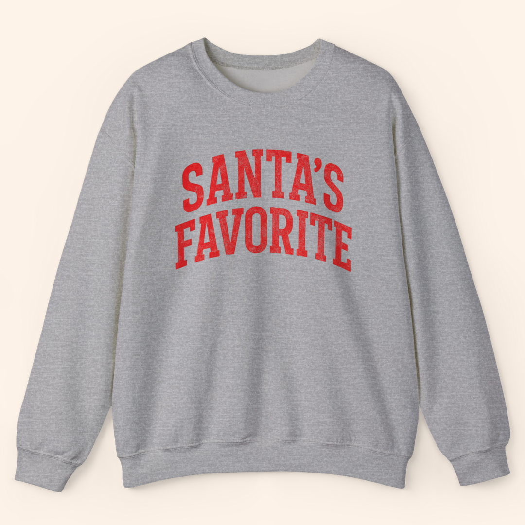 Heather gray Santas Favorite sweatshirt laid flat to show the full print and structure. Soft fleece body, ribbed trim, and bold holiday graphic lettering emphasize the cozy winter pullover design.