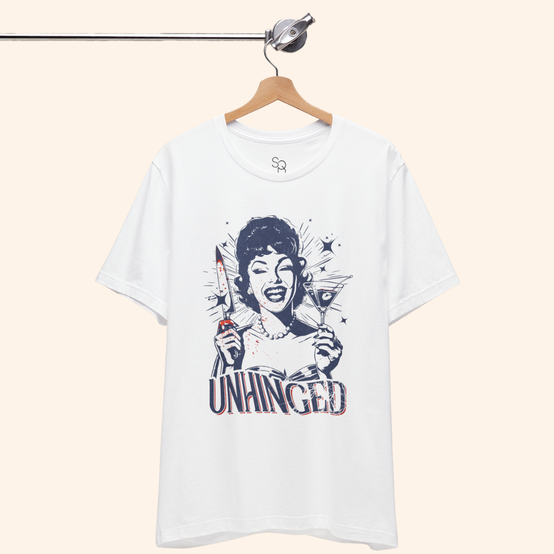Unhinged T-Shirt hanging on a wooden hanger from a minimalist metal rod, white tee draped naturally to show unisex fit and full front dark humor graphic, perfect for modern closet or boutique rack styling.
