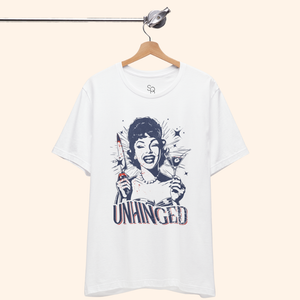 Unhinged T-Shirt hanging on a wooden hanger from a minimalist metal rod, white tee draped naturally to show unisex fit and full front dark humor graphic, perfect for modern closet or boutique rack styling.