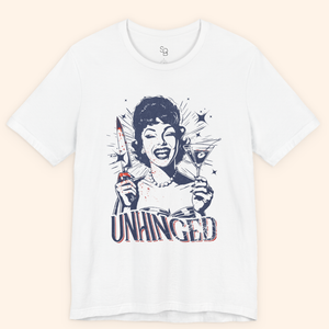 White Unhinged T-Shirt laid flat on a neutral background, showing a retro housewife holding a knife and martini with subtle red splatter and the word Unhinged in bold letters, dark humor graphic tee for streetwear style.