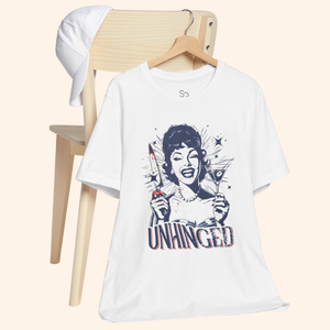 Unhinged T-Shirt hanging from a wooden chair with a white cap in the background, casual lifestyle setup that highlights the retro housewife knife and martini artwork, ideal graphic tee for off duty outfits and brunch plans.