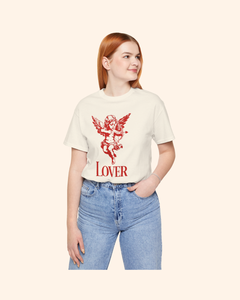 Mid length view of a woman modeling a natural color lover graphic t shirt with red cupid design, paired with blue jeans.