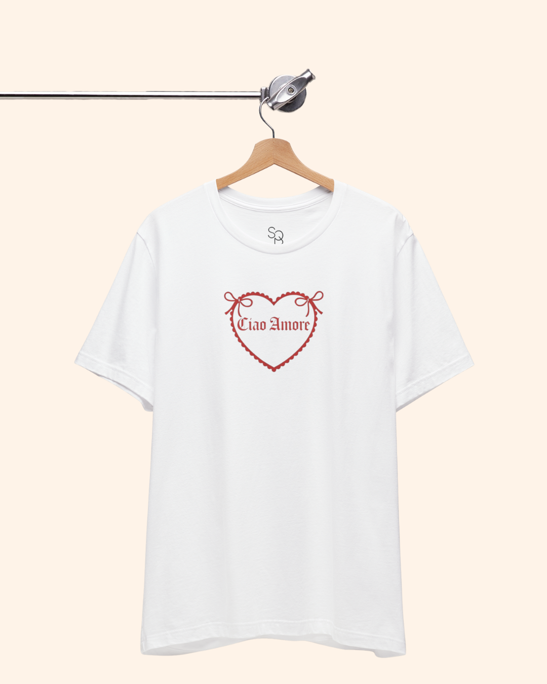 White unisex graphic tee hanging on a wooden hanger, featuring a red heart design and Ciao Amore phrase, styled in a clean street style aesthetic.