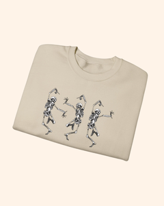 Folded Sand Three Is Company sweatshirt showing three dancing skeletons