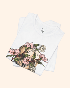 Folded white Spring With You tee showing pink blossoms and botanical skull design