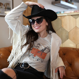 Woman wearing a black cowboy hat and sunglasses, sitting on a brown couch.
