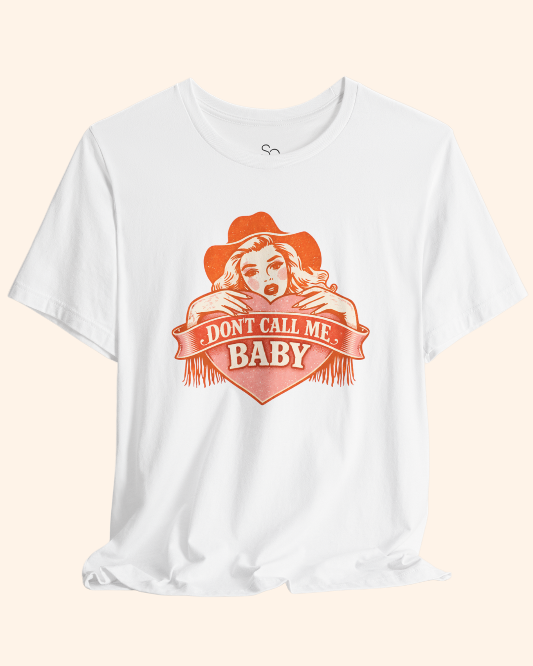 Close up view of the Dont Call Me Baby graphic showing an orange heart illustration with western style lettering printed on a white cotton t shirt.