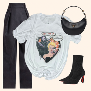 Hang Up Tee styled with tailored trousers, heeled boots, and a black crescent bag for a sleek Halloween horror-inspired streetwear look. Graphic features a retro blonde woman and masked slasher in a heart-shaped frame. Great for spooky season or edgy casual outfits. Soft poly-cotton feel. Unisex fit. Bella Canvas.
