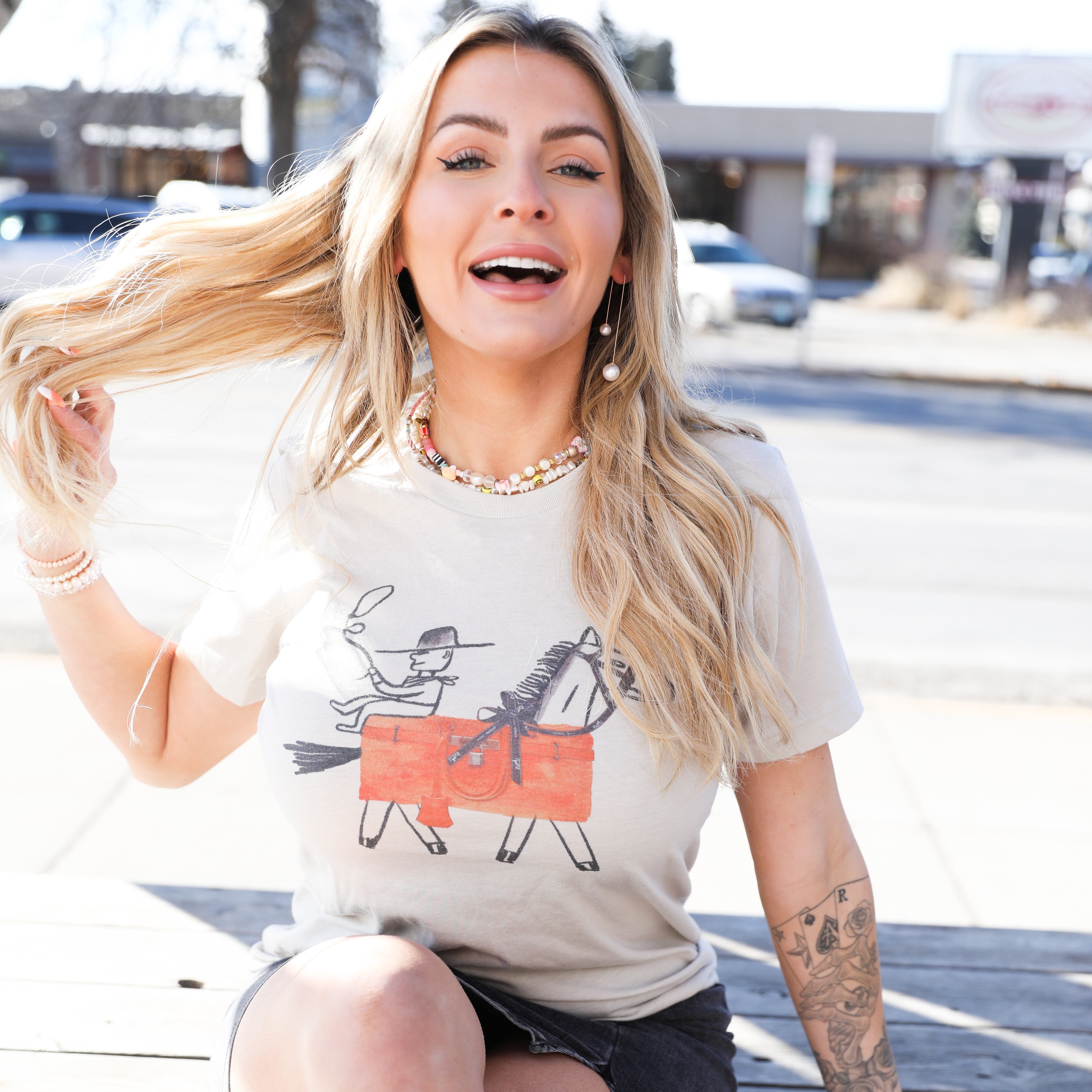 Cowgirl tee worn with black skirt and white boots. Outdoor photo shows playful, relaxed Western vibe.

