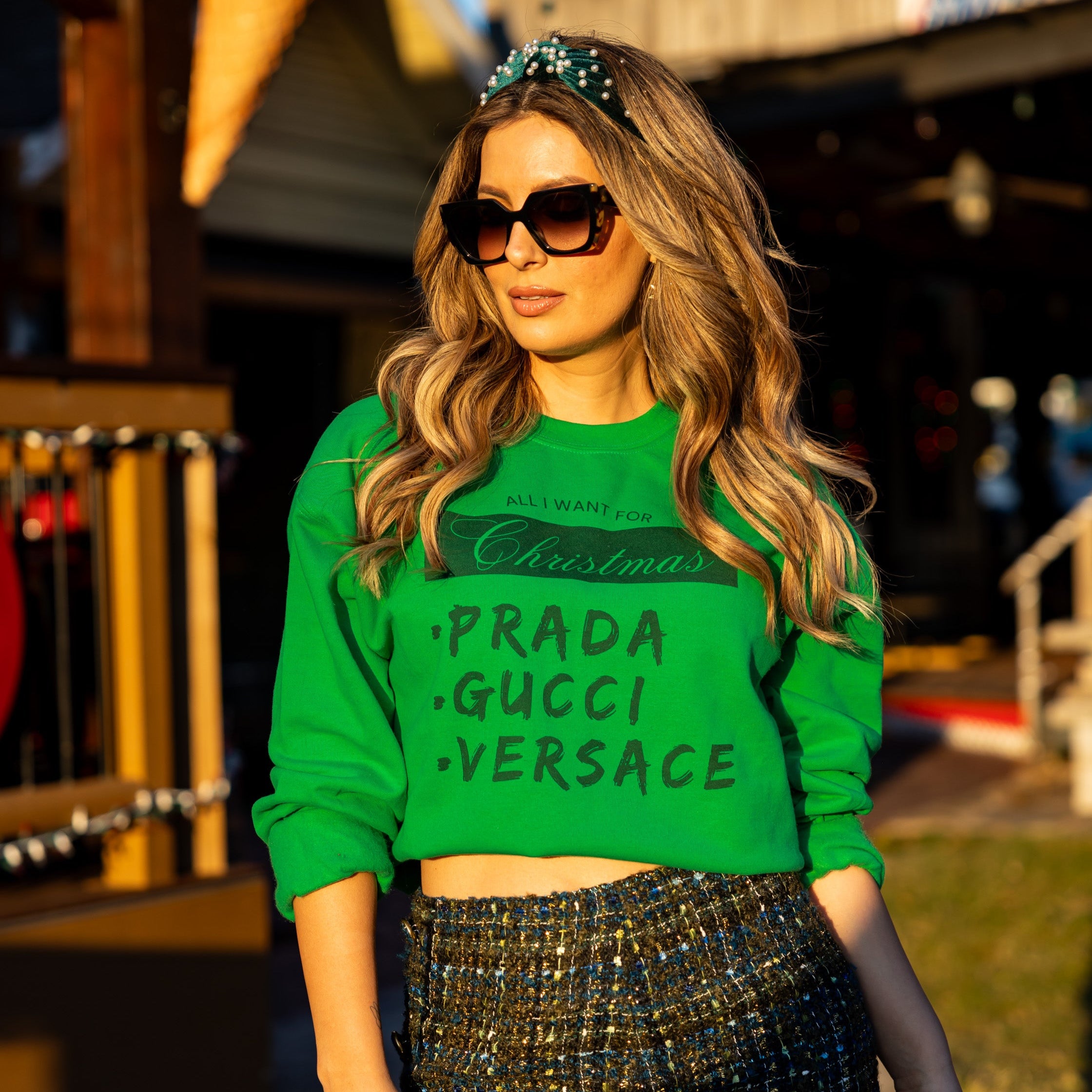 Woman in green cropped Christmas sweatshirt with fashion wishlist print, styled with sparkly mini skirt and green platform heels – chic holiday party look.

