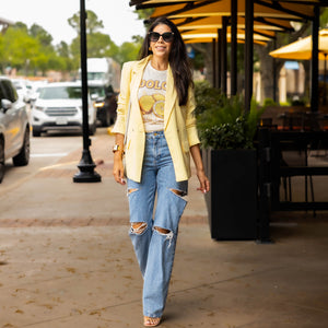 Woman wearing Fresh Start graphic tee with lemon print and “DOLCE” text — styled with ripped jeans and yellow blazer for a casual retro boho outfit in an outdoor city setting