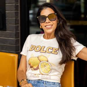 Close-up of woman sitting outside in sunglasses and DOLCE lemon graphic tee that says “everyday is a fresh start” — casual chic with gold hoop earrings and light wash jeans