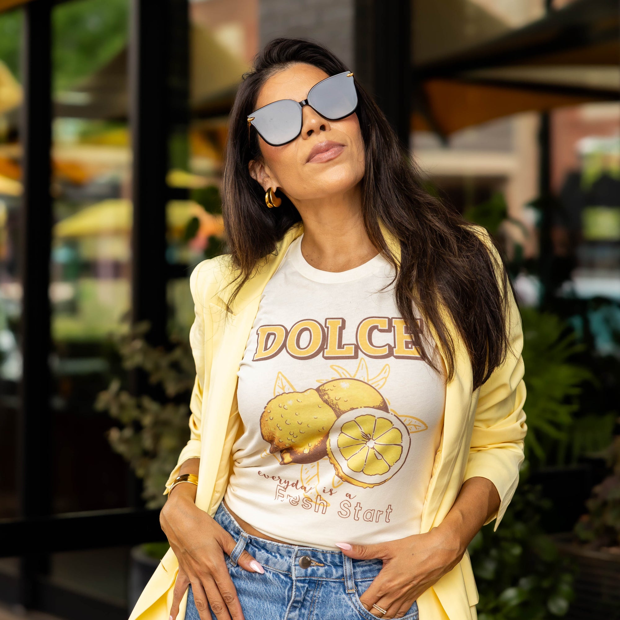 Woman wearing Fresh Start graphic tee with lemon print, light yellow blazer, and denim jeans — styled women's retro boho shirt outdoors
