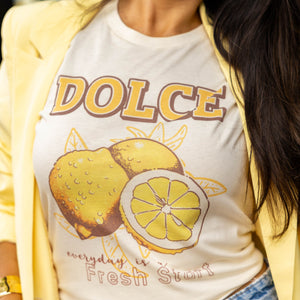 Close-up of woman wearing the “Fresh Start” lemon graphic tee with the word DOLCE above a bold yellow lemon print, styled under a light yellow blazer — perfect for spring and summer casual style.