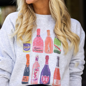 Close-up of champagne bottle sweatshirt styled with navy skirt, pink purse, and layered jewelry. Chic holiday or party detail.

