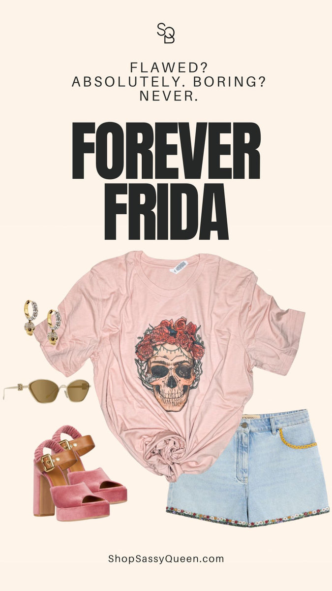 Flat lay of a pink skull graphic tee styled with light wash embroidered denim shorts, chunky pink velvet heels, gold hoop earrings, and oversized tan sunglasses, against a beige background with bold “FOREVER FRIDA” text and slogan: “Flawed? Absolutely. Boring? Never.” at the top.